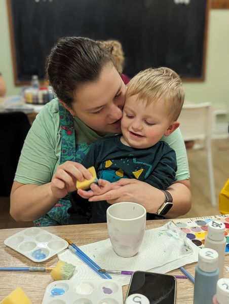 A mother and her child on her knee at a pottery painting session. The mother is wiping paint from her sons fingers