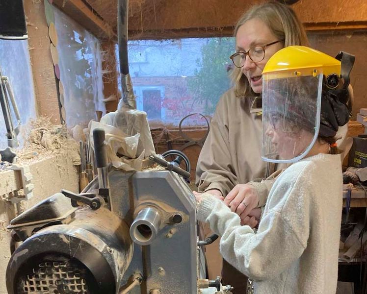 A girl being taught to woodturn at the lathe.