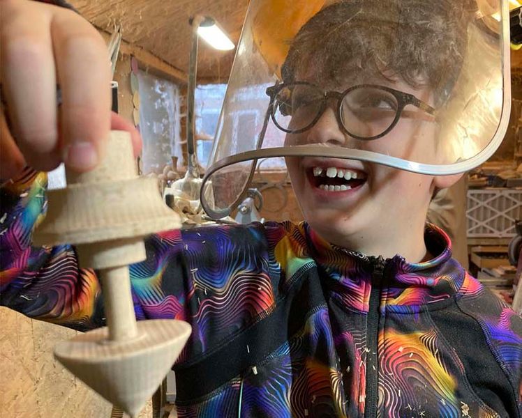 A boy holding his part turned wooden top.