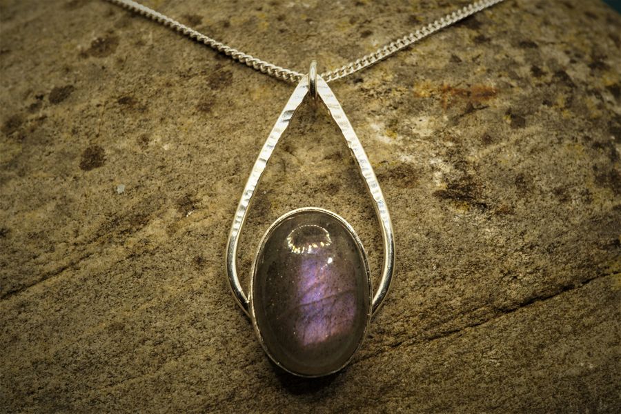 Purple labradorite pendant with silver teardrop surround against a stone background