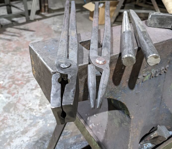 Flat bit tongs (fullered), next to scrolling tongs, a round tapered punch and a square tapered punch