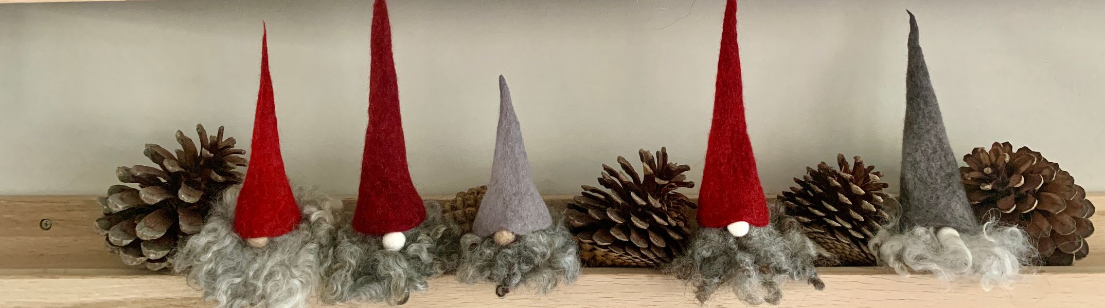 A selection of Scandi Tomte with shades of red and grey conical hats of varying heights.  They have long curly beards.  There are pine cones between them.