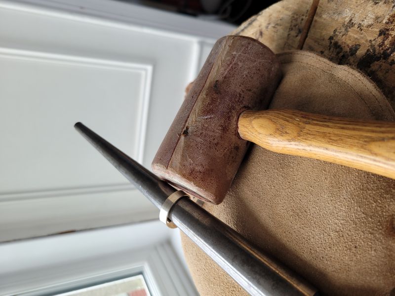 Silver ring on a mandrel and a rawhide mallet for shaping it.
