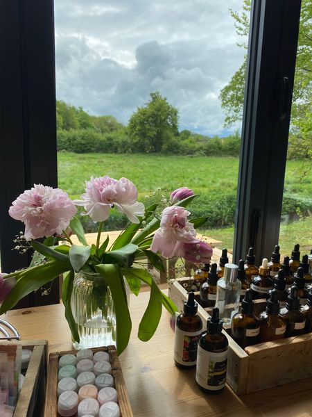 Essential oils on a table next to pink flowers with a view of fields behind