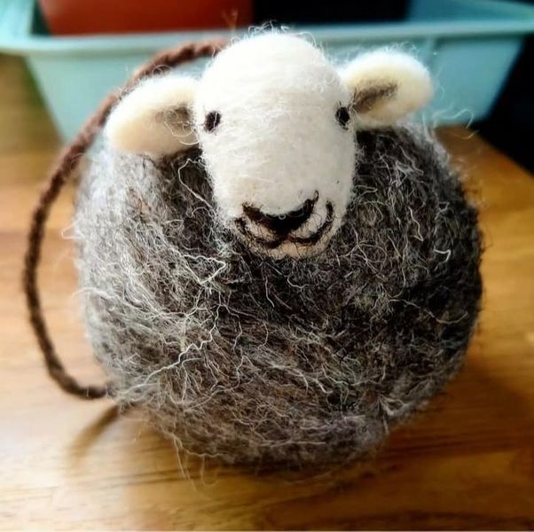 A felted sheep with a grey body, white head and smiley face.