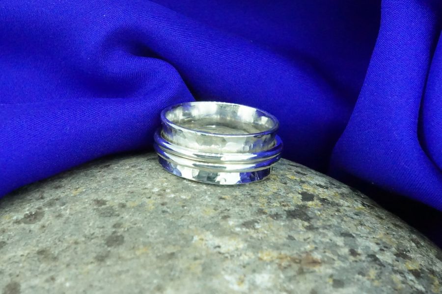 Silver wide two spinner ring sitting on a rock against a blue satin background