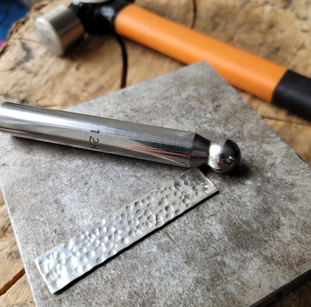 A sterling silver ring band for a spinner ring being textured with a punch and hammer on a steel block.