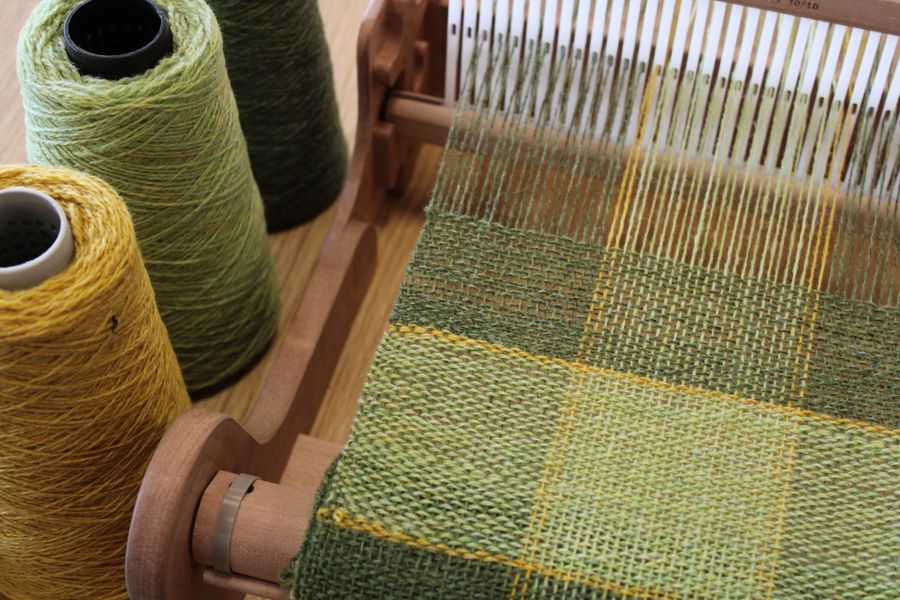 A scarf on a loom with green and yellow yarns