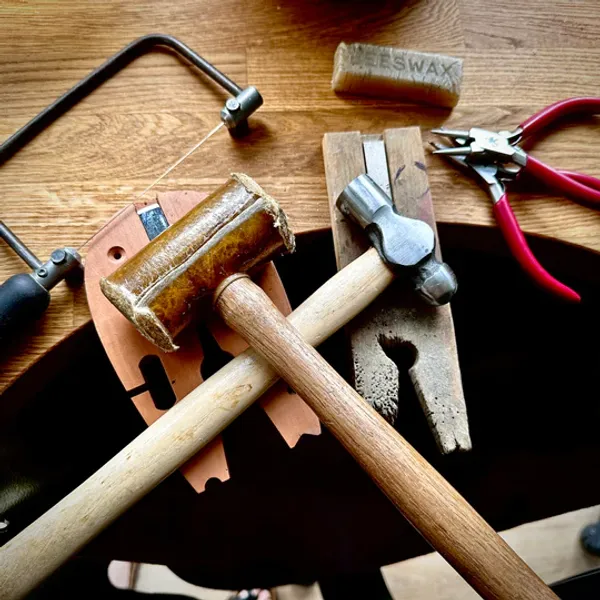 Metalsmith tools, including a jewelers sawl, leather hammer, steel hammer and pilers.
