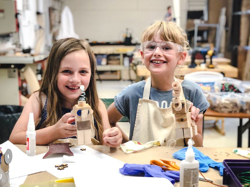 Two girls proudly show off their wooden characters built at an Ash & Co. Workshops mini-maker woodworking session for kids