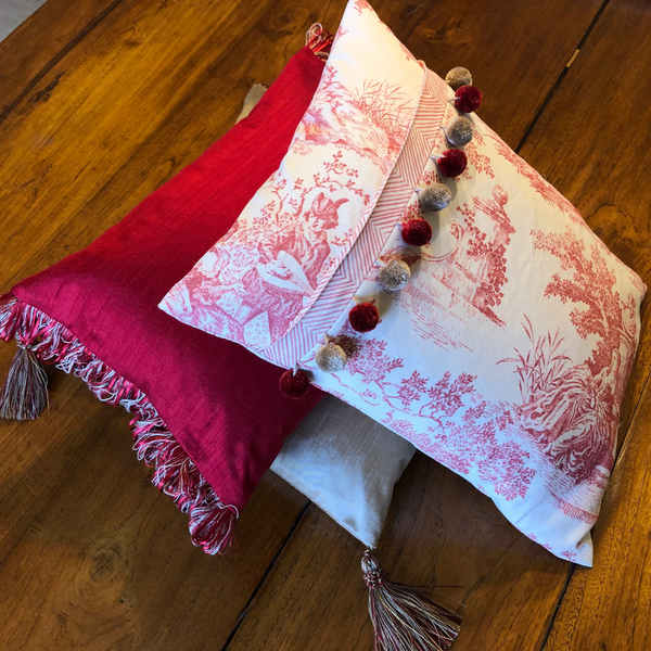 Bespoke scatter cushions in hues of red and cream with pom pom and ribbon trim