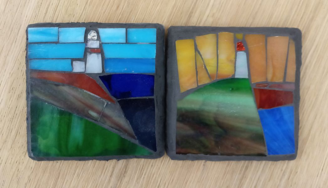 Two lighthouses in stained glass on slate.
