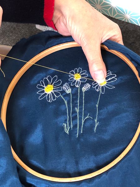 Hand sewing beads onto a stitched flower picture
