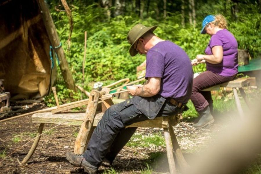 Sitting on a shaving horse shaping parts for a chair.