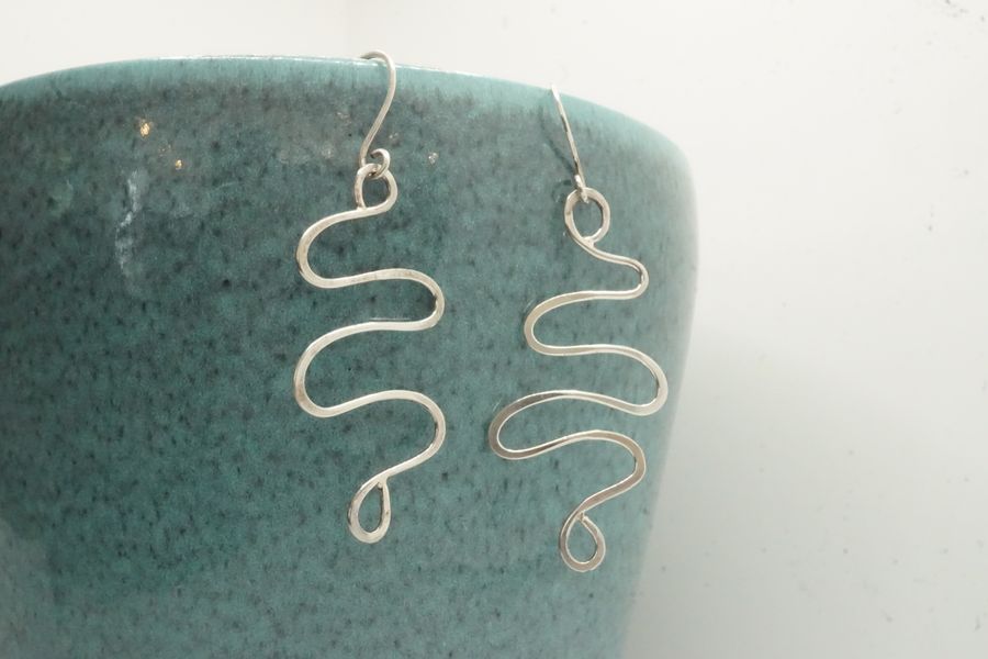 Wavy silver wire earrings on earhooks against a turquoise pot background