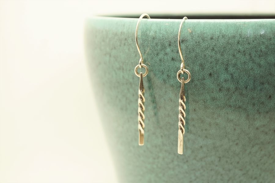 Twisted wire drop earrings in silver sitting against a turquoise pot background