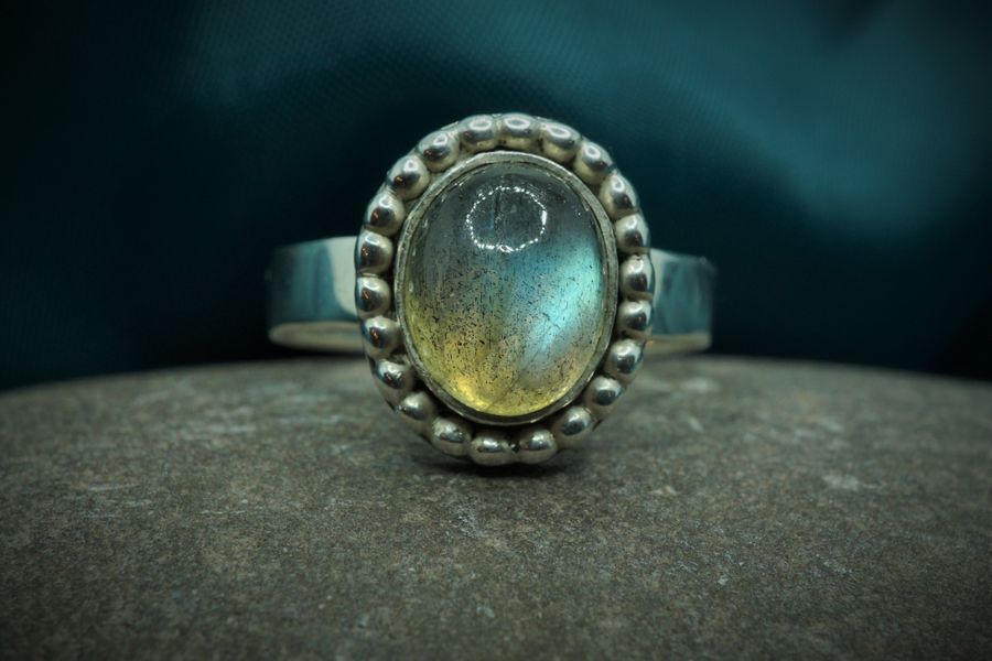 Labradorite green blue stone with beaded silver surround ring sitting on a stone background