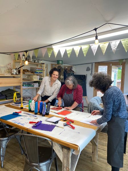 three ladies print their lino cuts in a wooden studio with bunting
