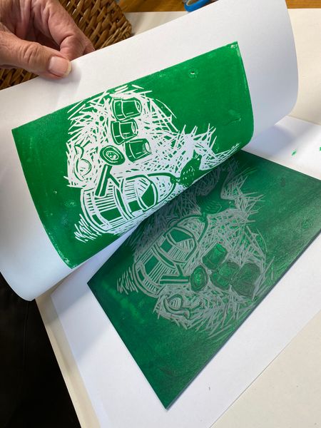 Paper being pulled back to reveal a green lino print