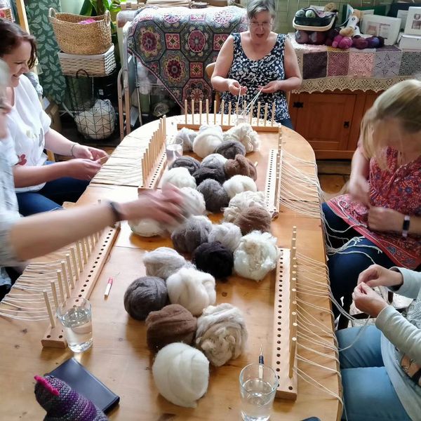 People around the table, warping their looms.