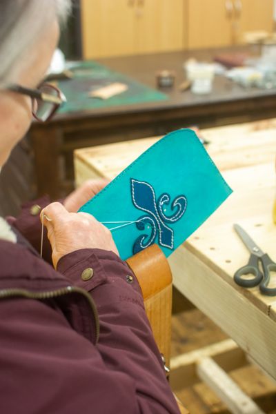 A student sewing a flur-de-lis on a blue leather bag