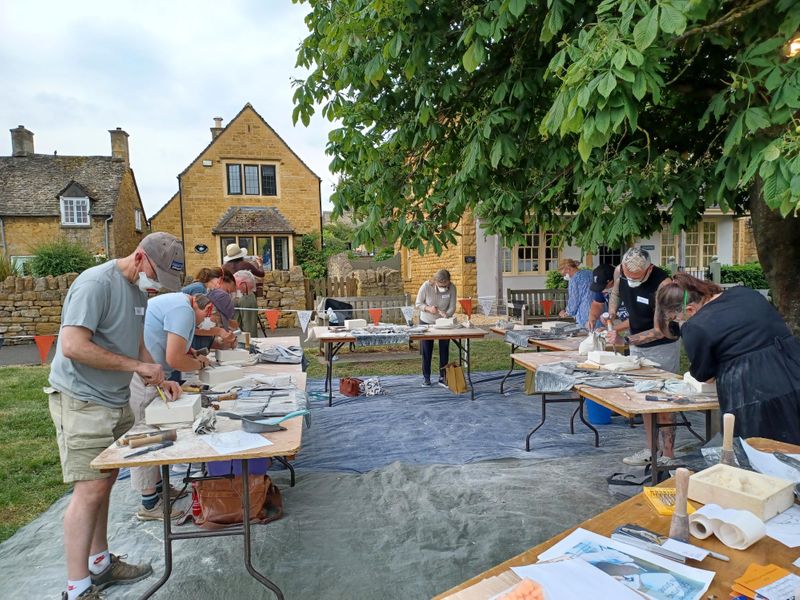 10 relief carvers in the shade of a tree.