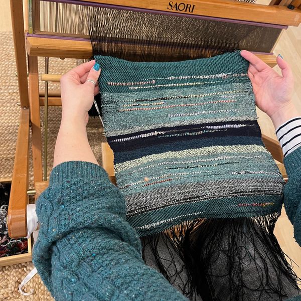 View from weaver's perspective. Green cloth held between two outstretched arms over the loom. 