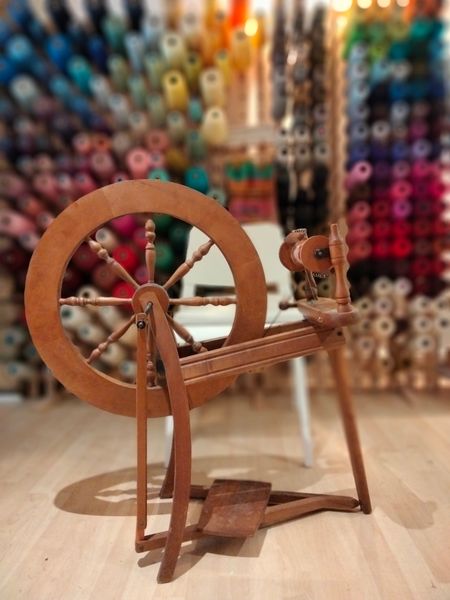 A spinning wheel in front of cones of yarns at Wayward Weaves Studio